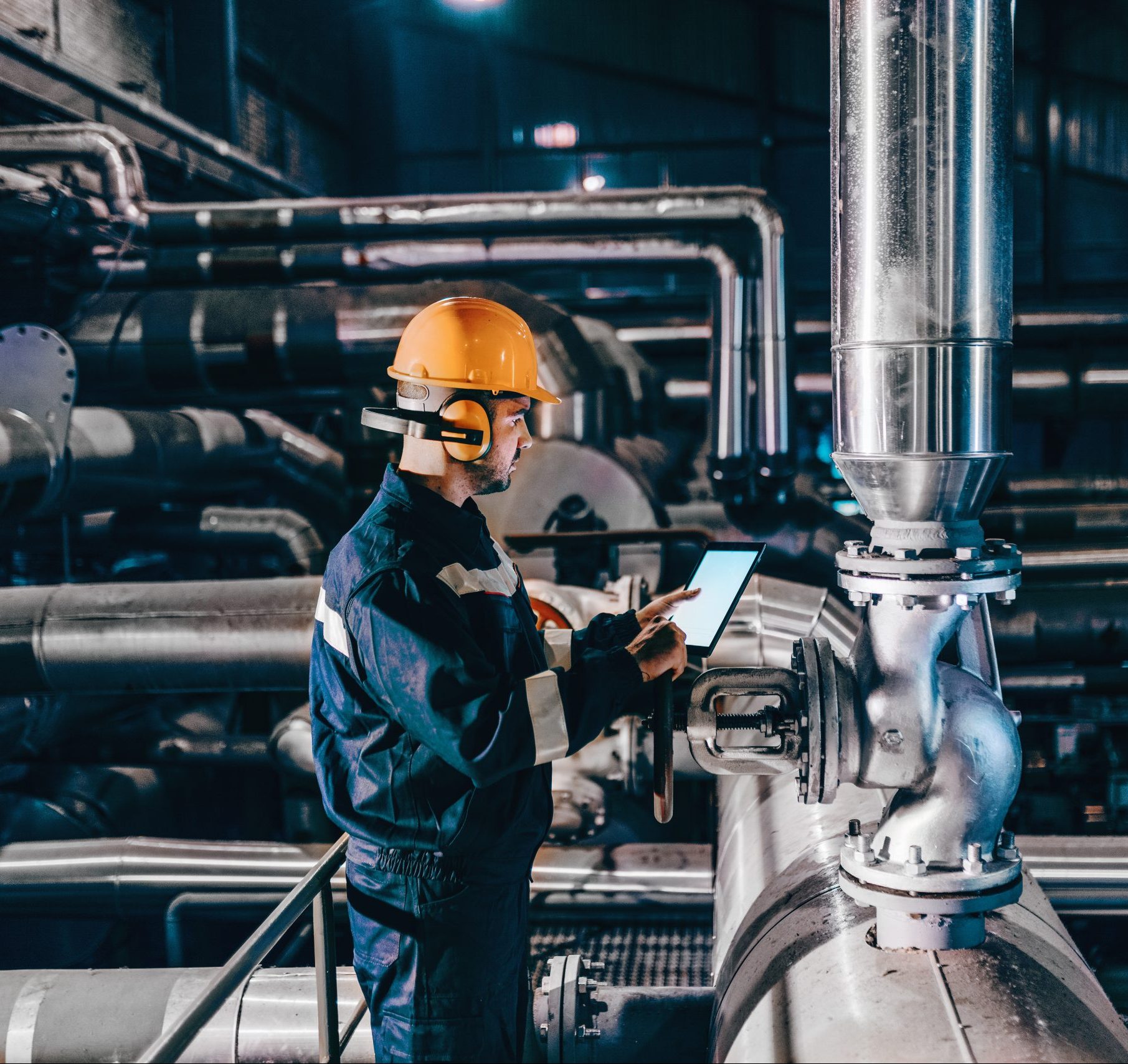 Técnico industrial revisando maquinaria con una tablet de medicion en una planta de procesamiento.